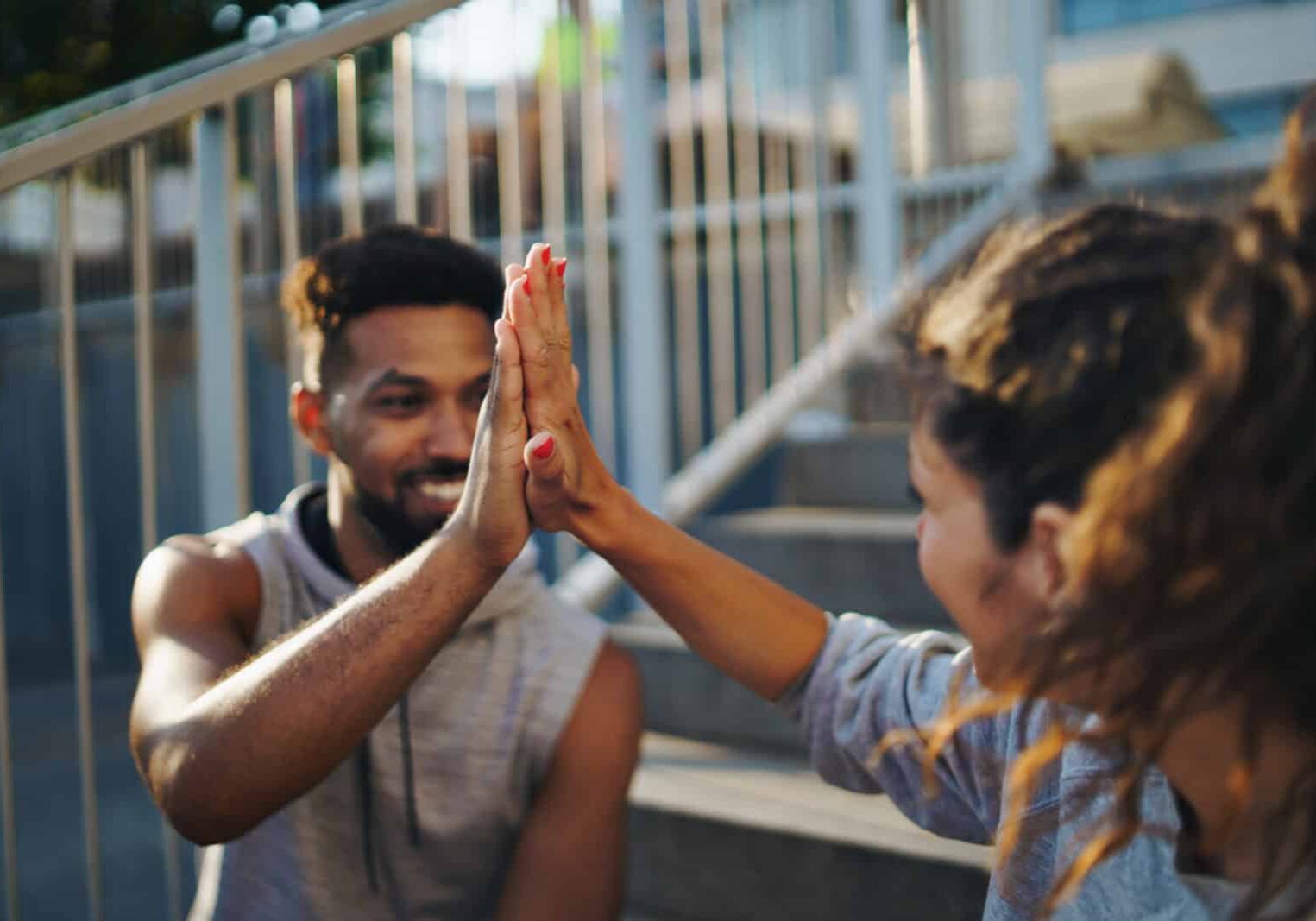 Man and woman friends resting after exercise outdoors in city, giving high five.